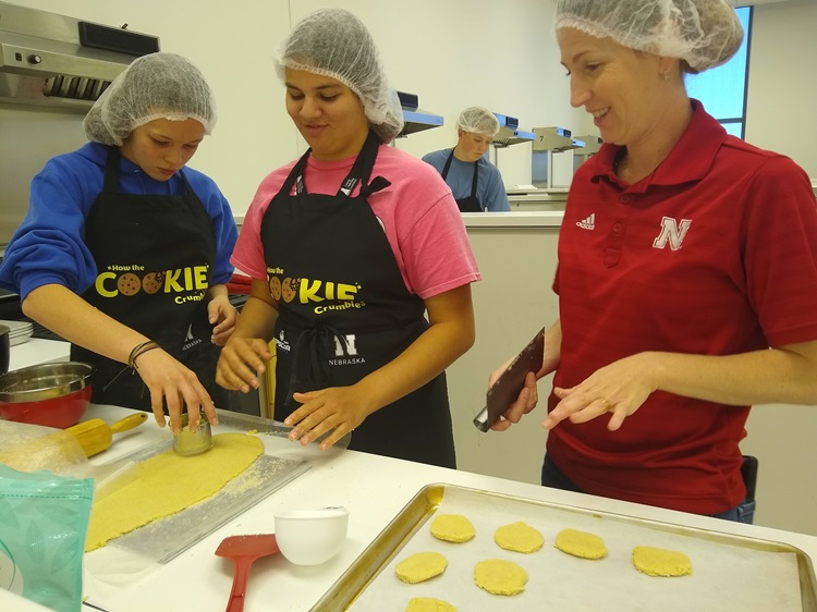 A professor teaches students about recipe formulations while two students roll out cookie dough