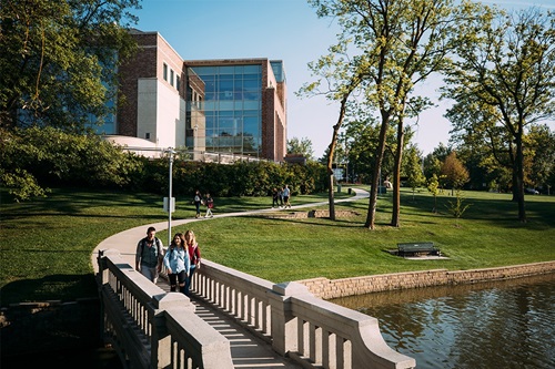 View of the beautiful Doane university campus with students crossing a bridge over a lake.