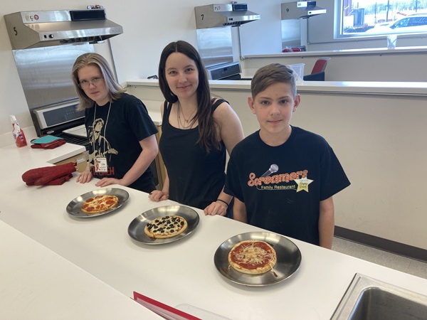 Three students stand by their pizzas they made from scratch